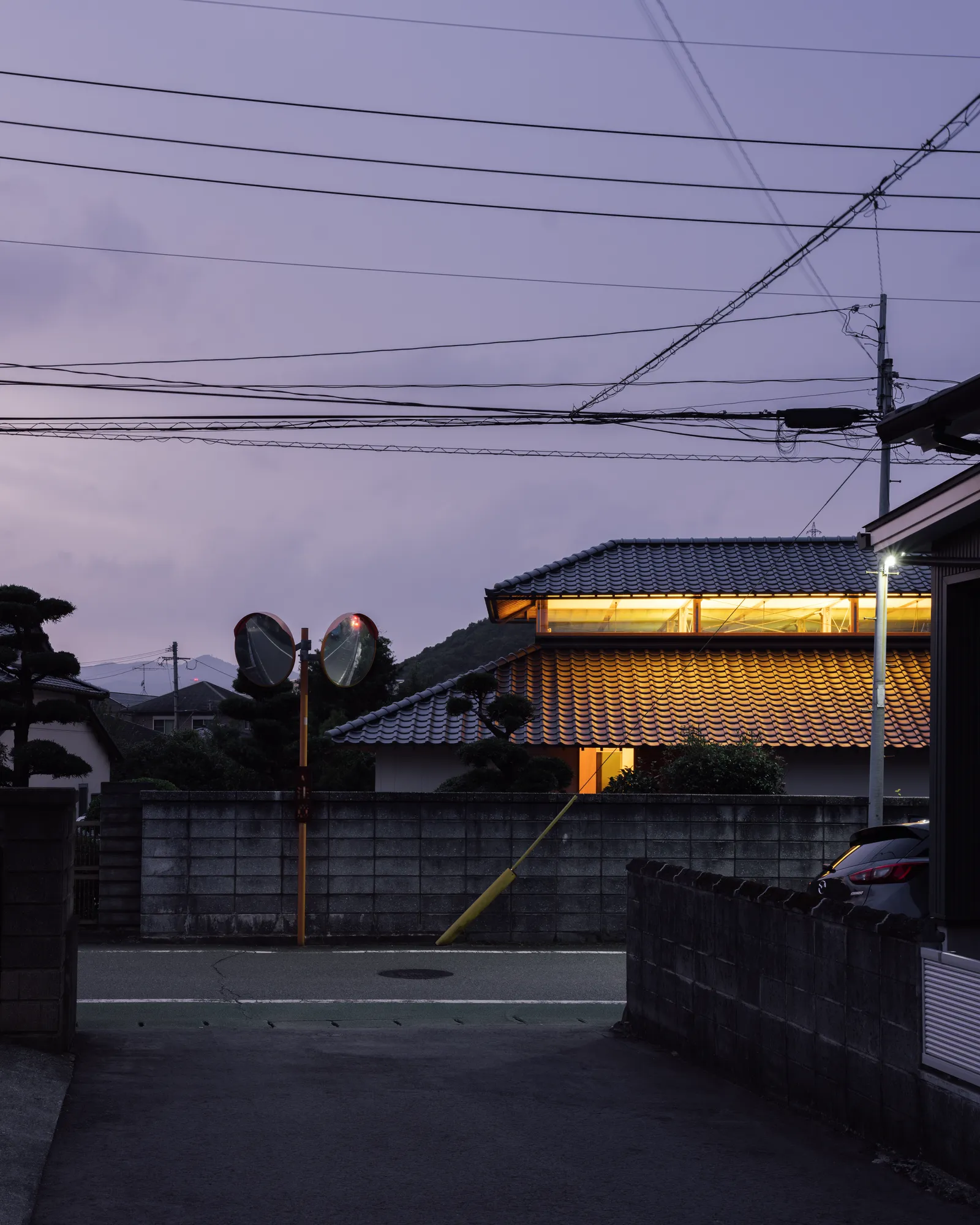 夕景のなか、越屋根の開口から漏れる光が瓦屋根の表情をやわらかく浮かび上がらせる。