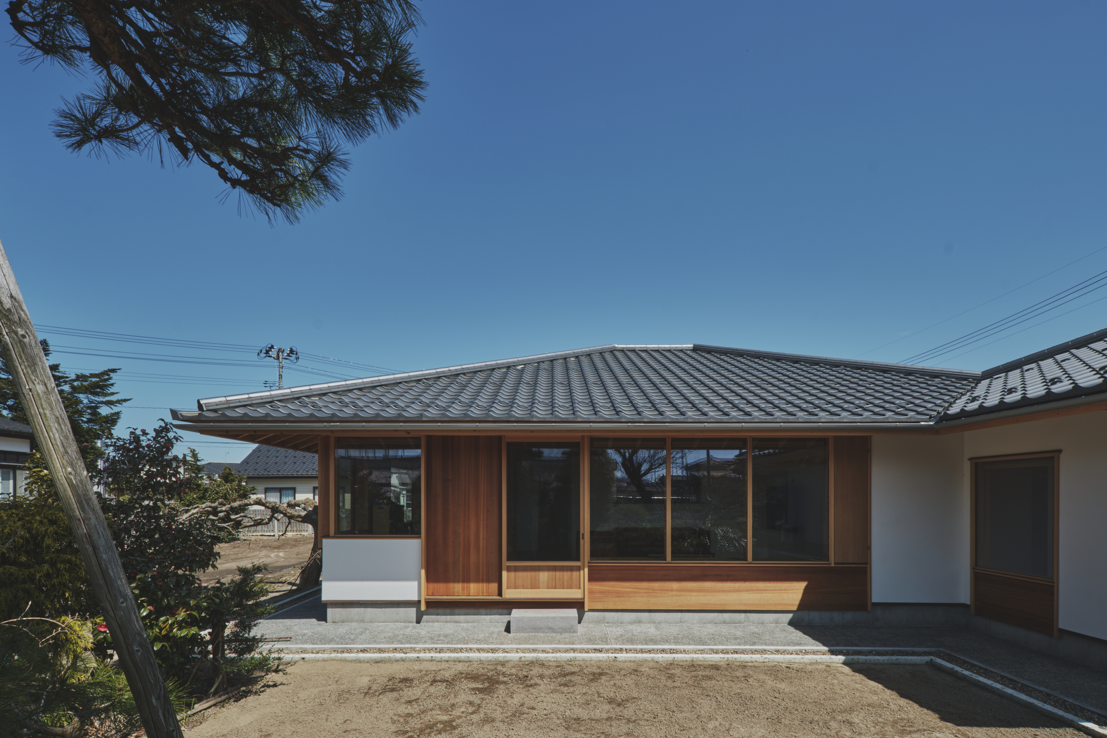 低く深い軒と寄棟屋根が、雪や海風の厳しい鶴岡の気候に応答する、落ち着きある住まいの表情をつくる。