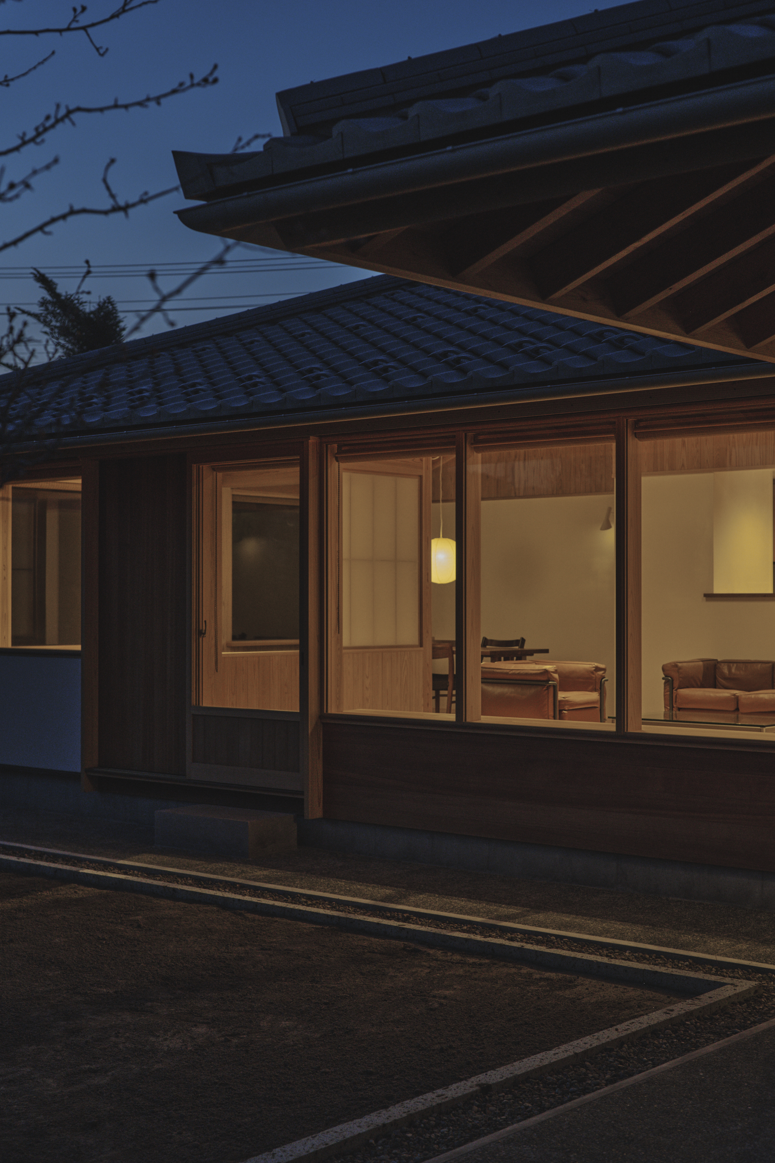 夕暮れの光の中、深い軒と瓦屋根が住まいの輪郭をやわらかく浮かび上がらせる『鶴岡の家』。