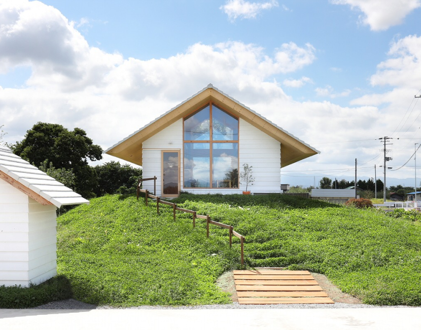 青空と緑の丘に建つ大きな窓のある白い切妻屋根の建物