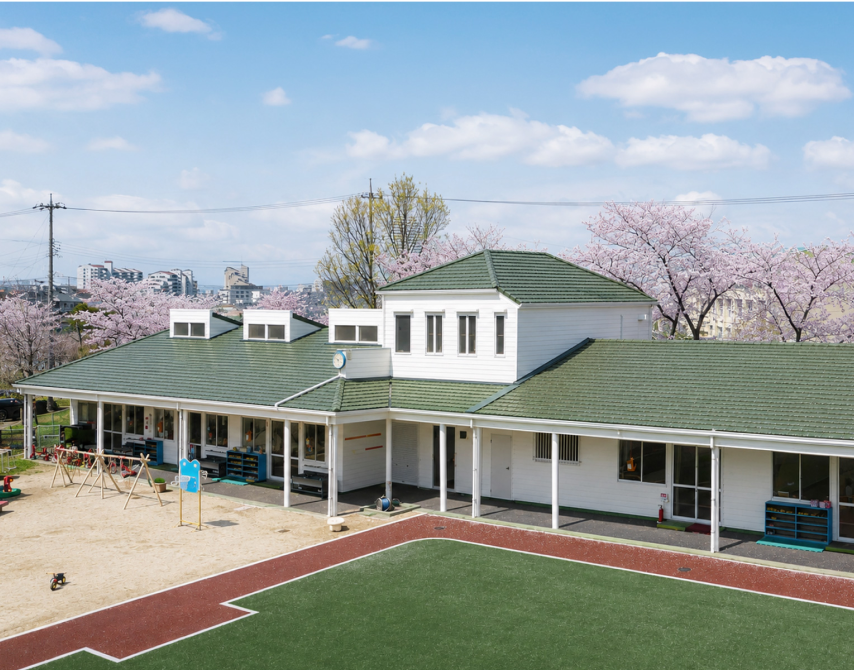 桜の風景に映える緑の瓦屋根の園舎外観（スーパートライ110 タイプIII）